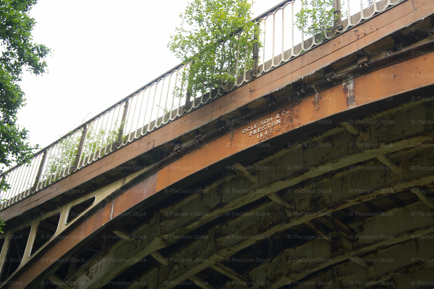 Bridge with metal railing and visible wear, surrounded by greenery.