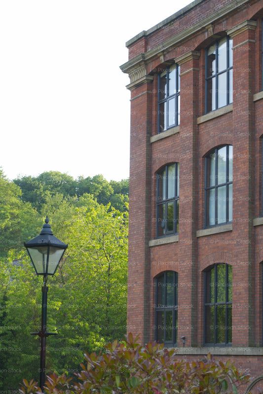 Brick building with large windows and a street lamp in front, surrounded by greenery.