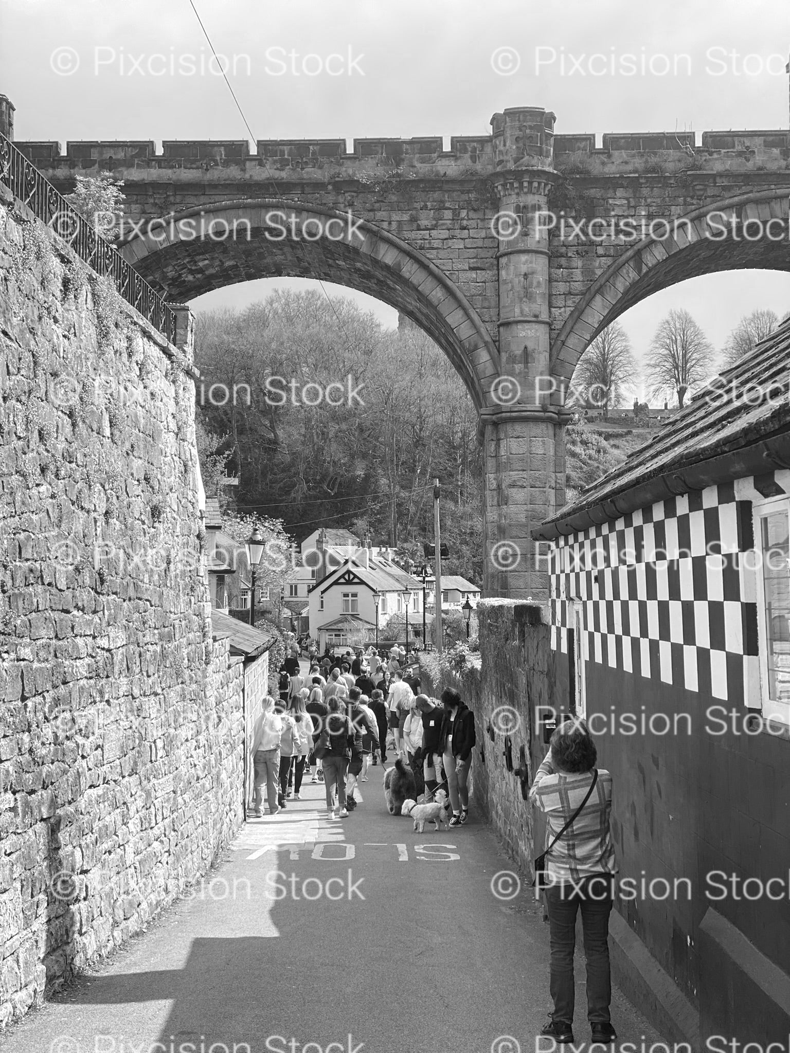 People Walking Beside a Tall Stone Viaduct Wall (Monochrome)