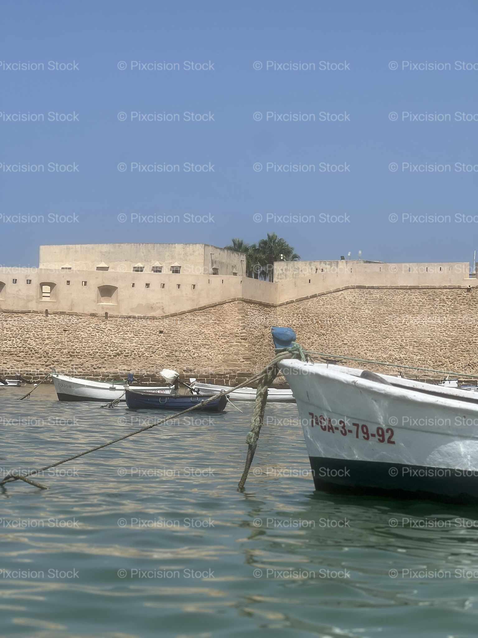 Traditional Fishing Boats Moored in Harbour with Historic Sandstone Castle Walls Cádiz Spain