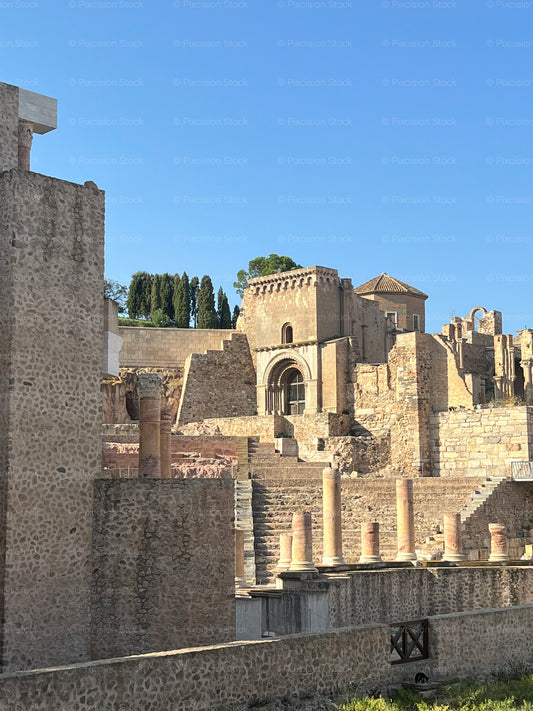 Ancient Roman Ruins with Medieval Stone Building Under a Clear Blue Sky