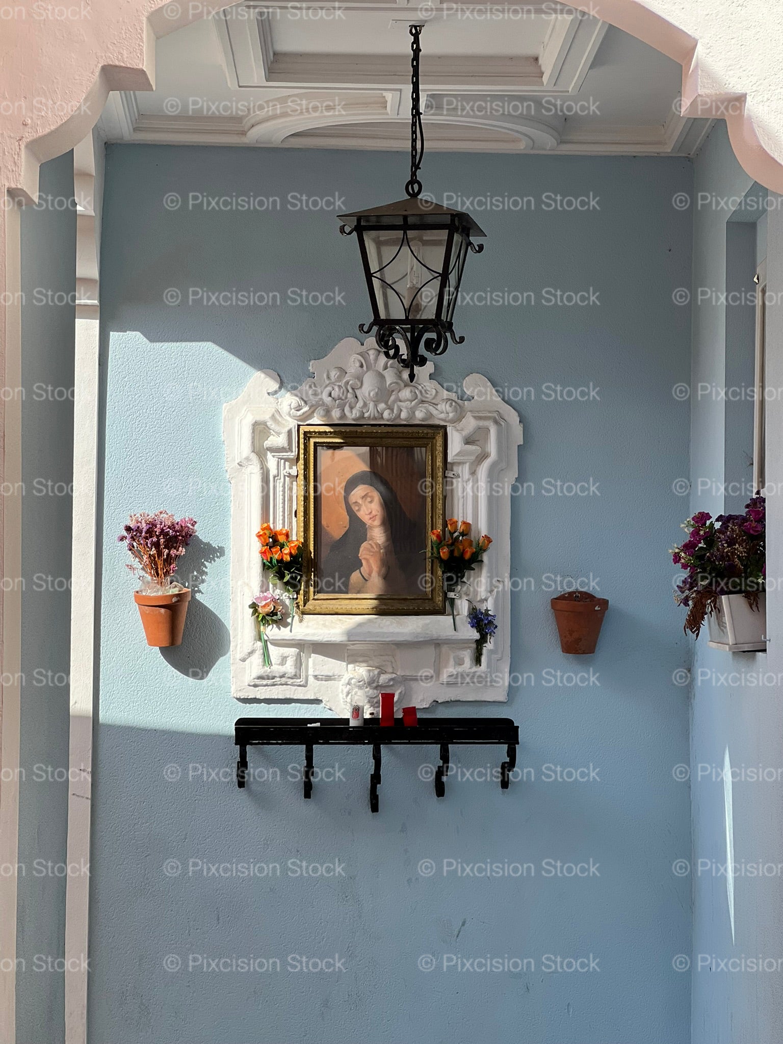 Traditional Spanish Street Shrine with Virgin Mary Painting and Flower Pots on a Blue Wall