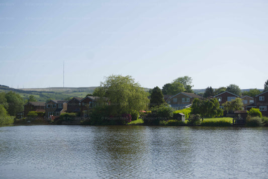 A scenic view of residential houses and green trees along the edge of a wide lake under a clear blue sky.