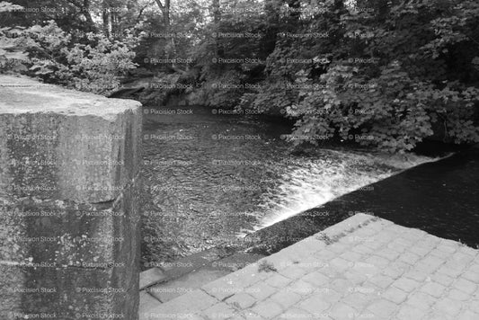 Stone Bridge or Weir Structure Along a Tree-Lined Riverbank (Monochrome)