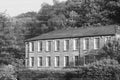 Long Two-Story Stone Building Nestled Against a Wooded Hillside (Monochrome)