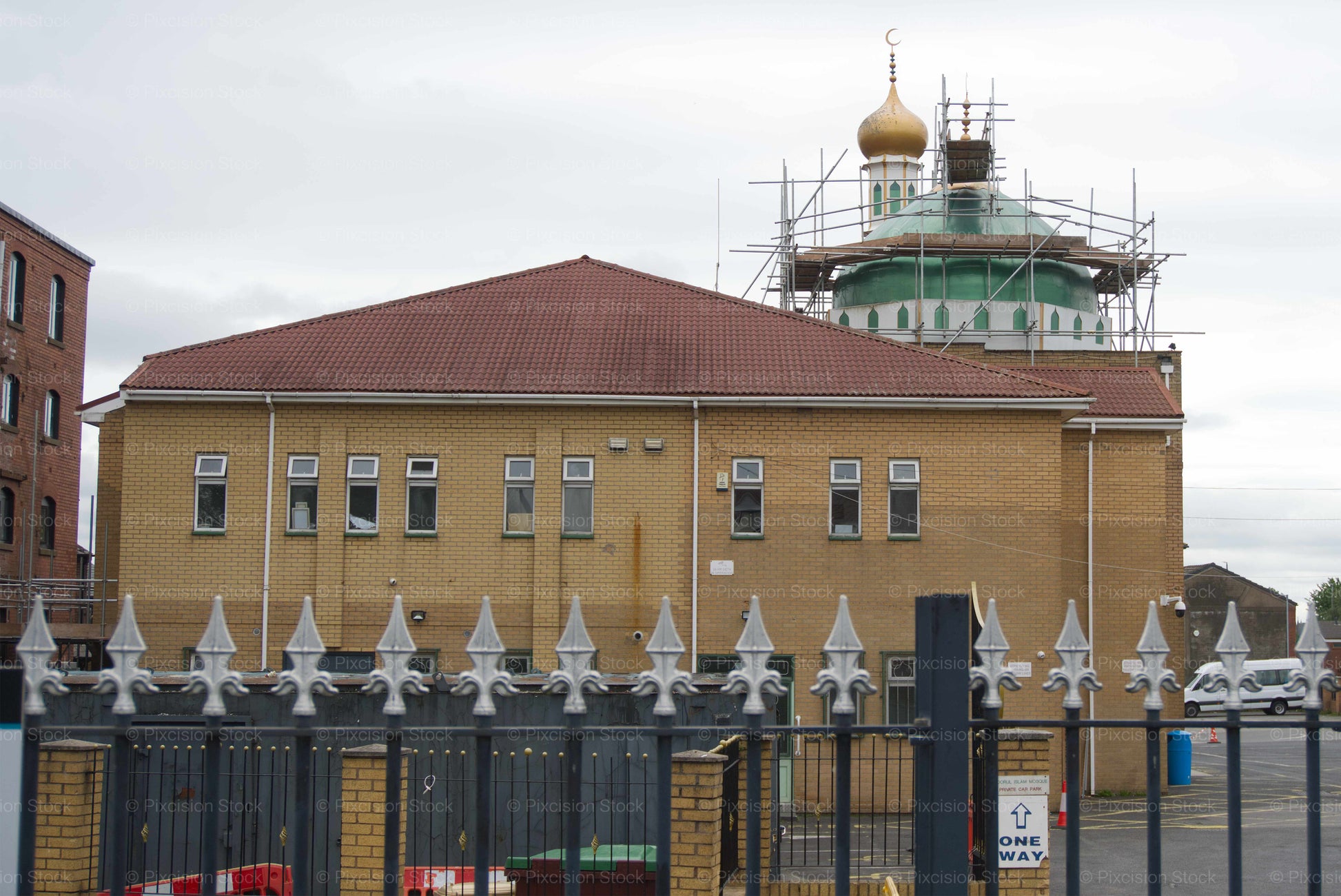 Building with a red roof and a domed structure in the background, surrounded by a fence.
