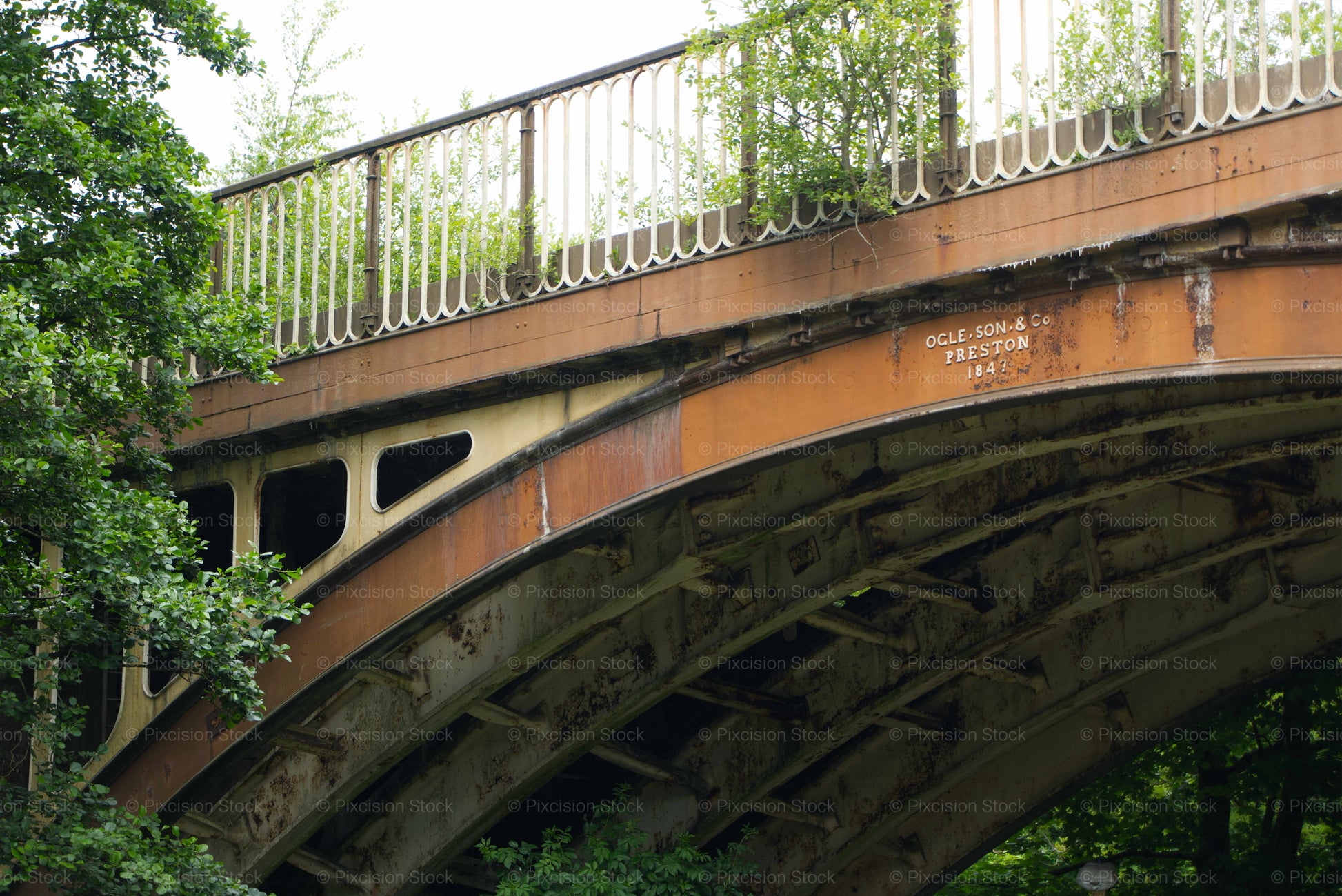 Curved bridge with metal railing and visible branding, surrounded by greenery