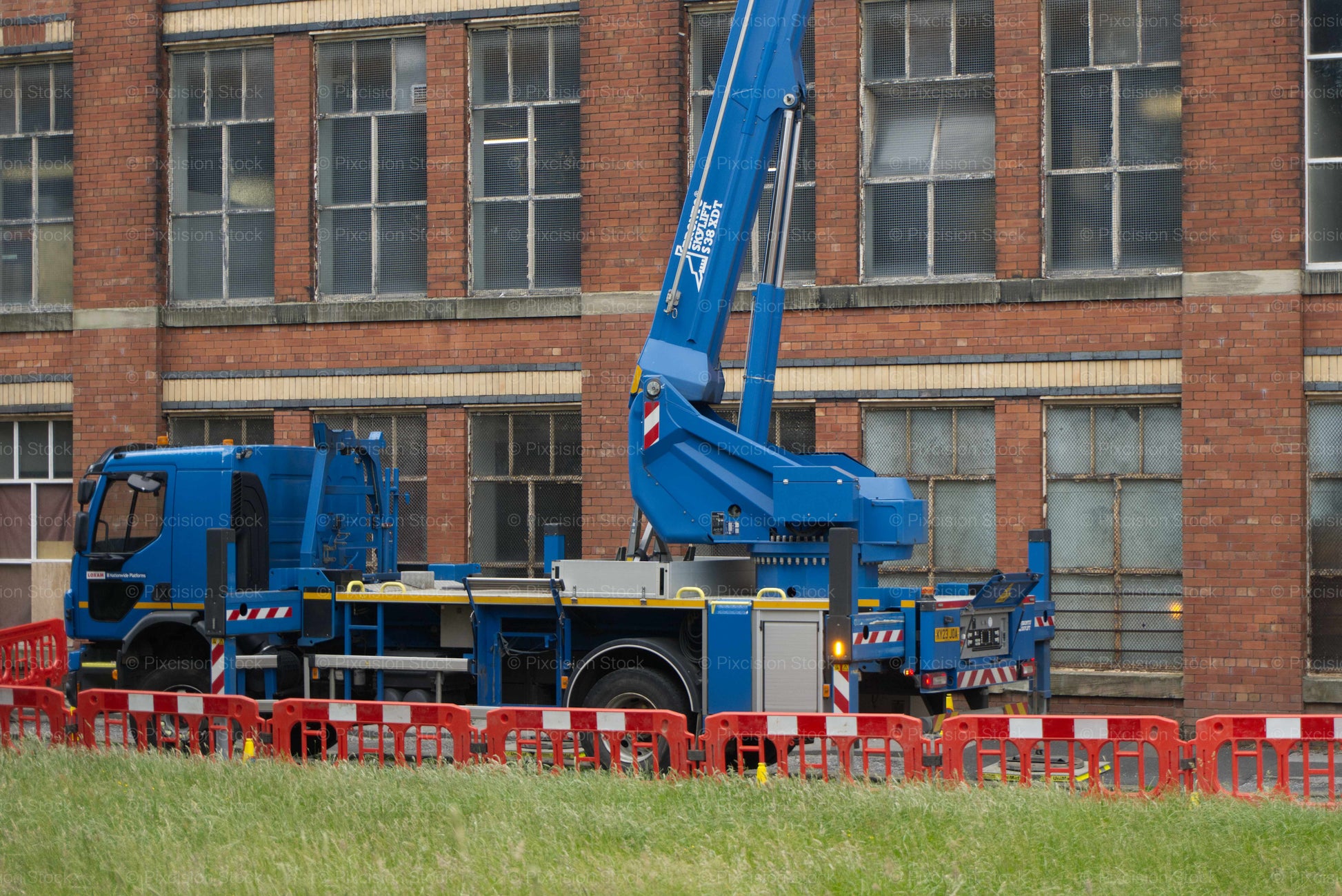 Blue crane truck in front of a brick building with red barriers.