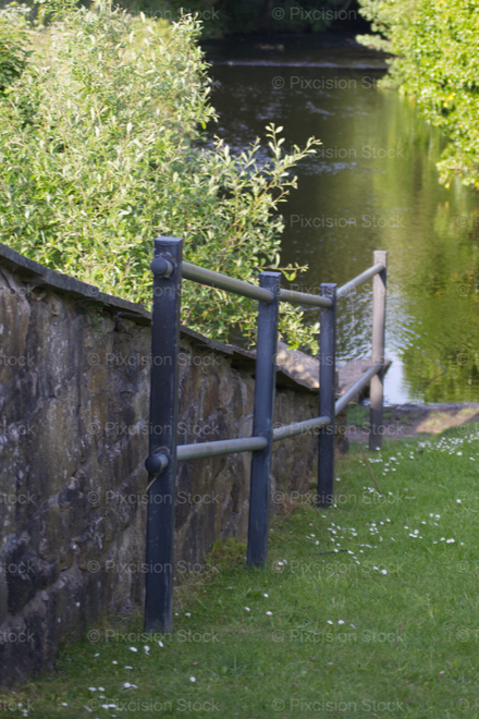 Stone wall with metal gate leading to a garden path by a river bank
