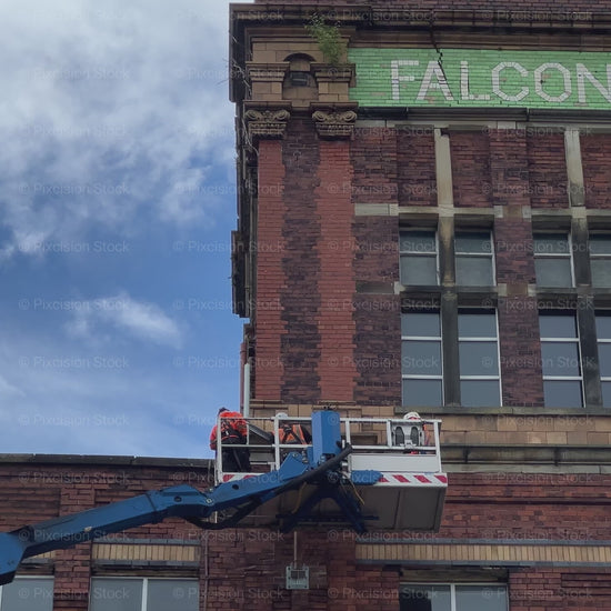 A video showing workers in a cherry picker lift inspecting the historic brick tower of Falcon Mill.