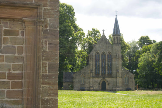 An exterior view of St Saviour's Church, an Anglican stone church in Radcliffe, England, framed by a stone wall in the foreground and surrounded by green trees.